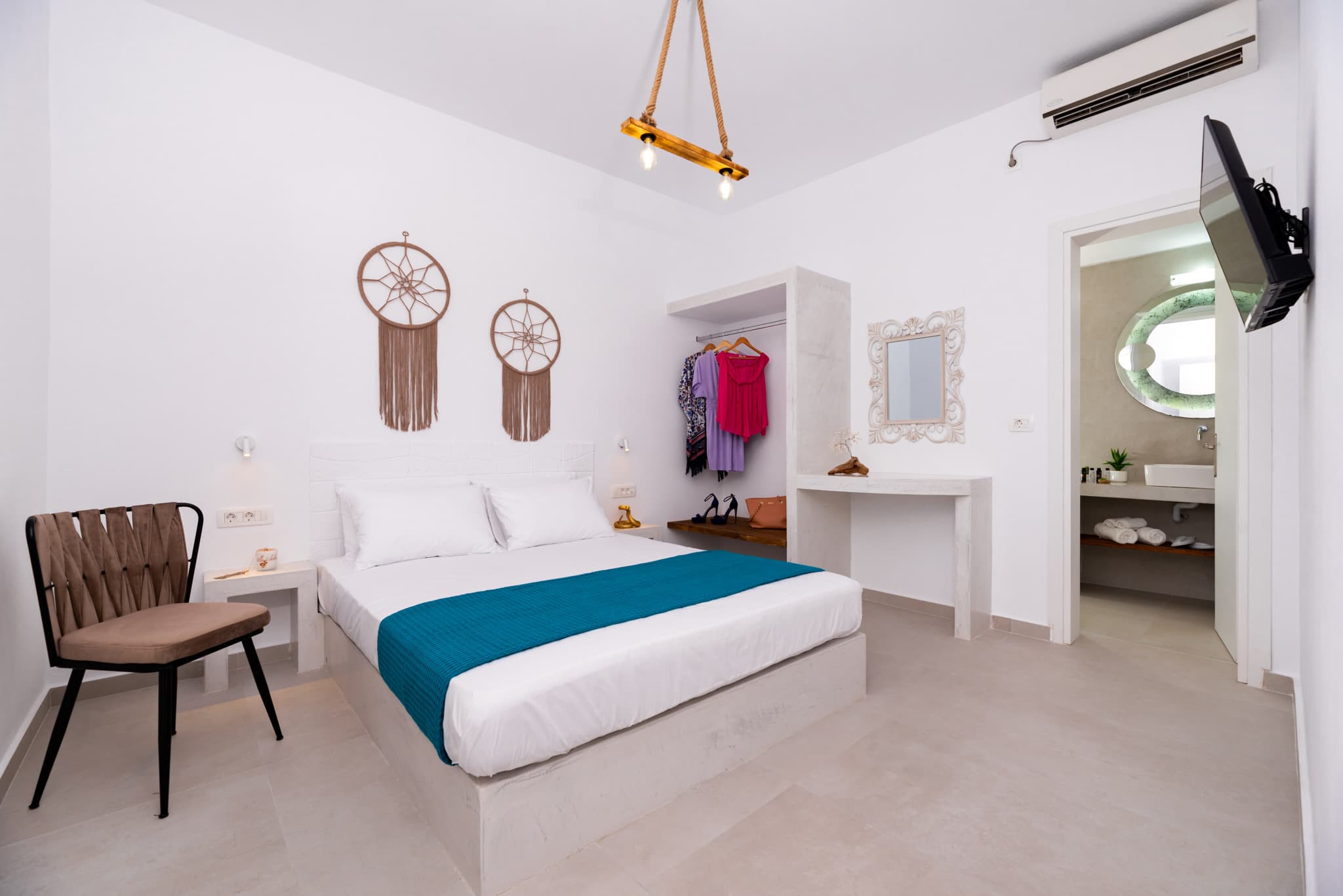 Modern white bedroom featuring a teal bed runner, dreamcatchers, and an open closet.