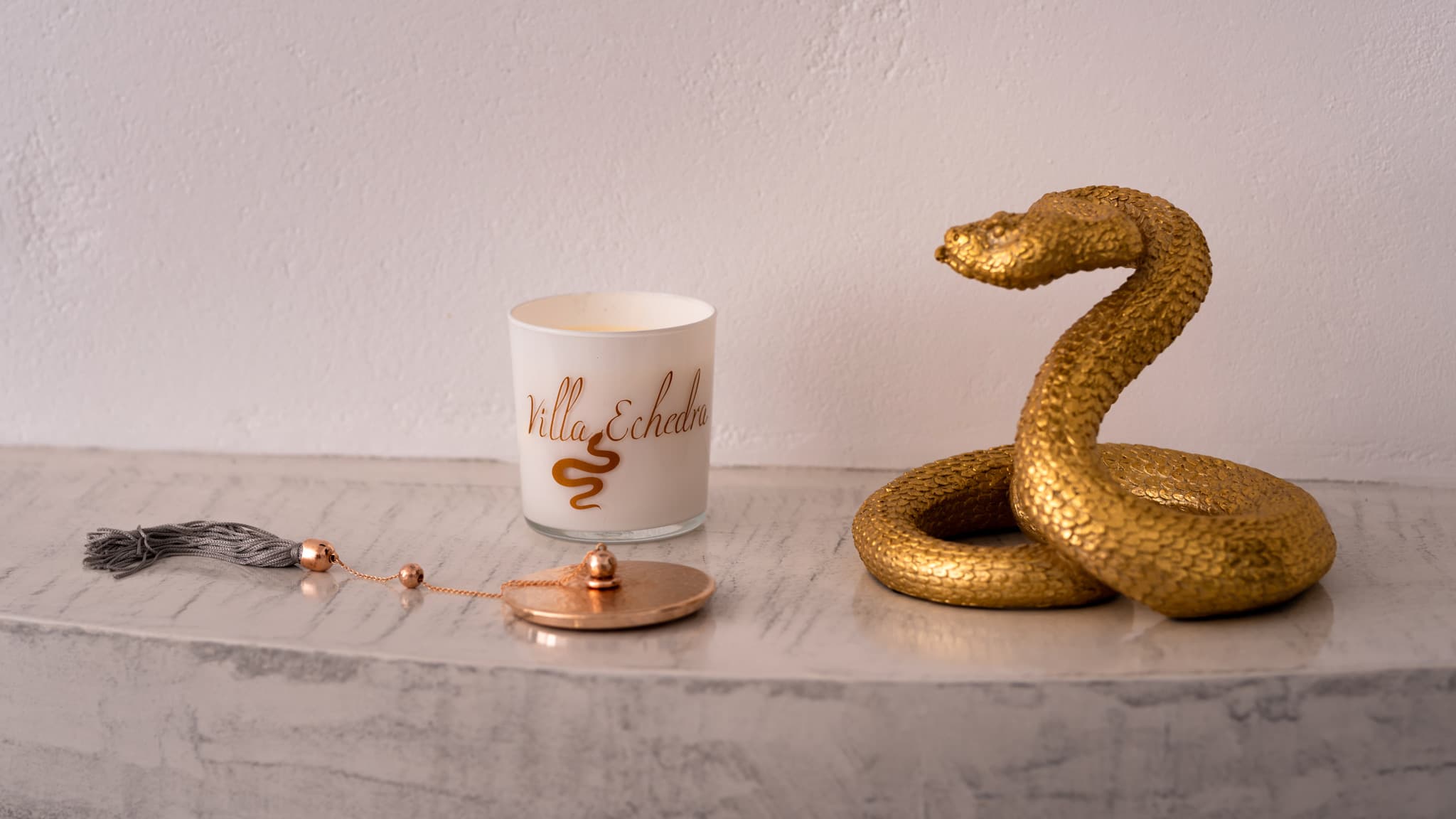 White Villa Echedra candle, gold snake figurine, and tasseled lid on a marble surface.
