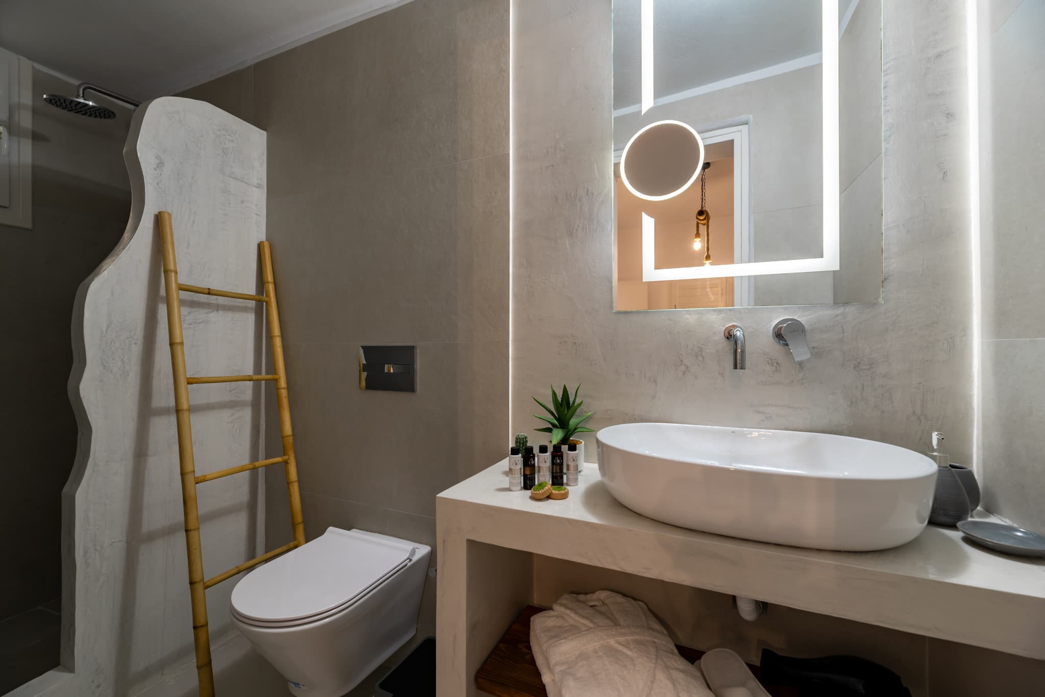 Modern bathroom with white vessel sink, backlit mirror, wall-mounted toilet, and bamboo towel ladder.